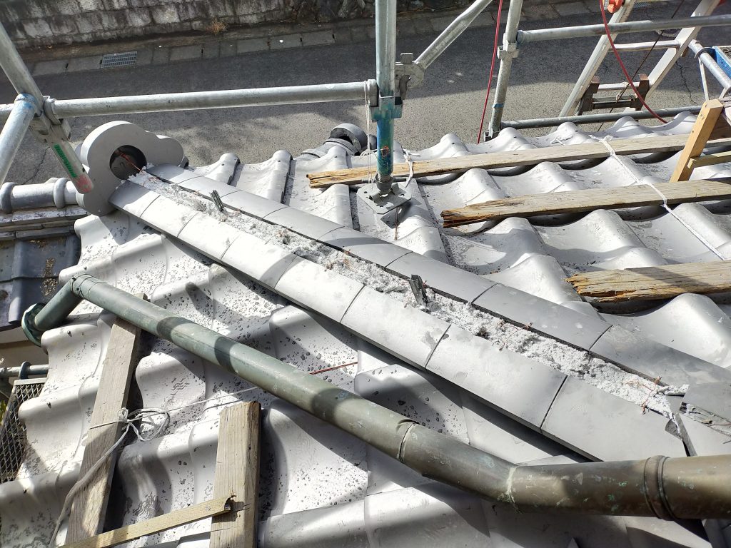 下屋根の瓦を一枚ずつ納まりを確認しながら葺き上げている施工中の様子